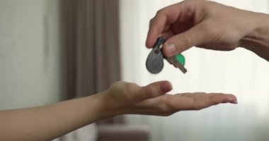 Erkek eli, kadın eline kapı anahtarlarını uzatarak sorumluluk ya da mülkiyet transferini gösterir. Doğal ışık, yakınlardaki bir pencereden süzülerek sıcak bir atmosferi yükseltir..