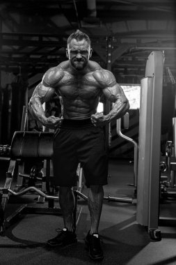 Sporcu adam spor salonunda kaslarını esnetiyor. Etrafı sarılmış spor aletleri ayarlıyor. İdeal sağlık için egzersiz yaparken güç ve adanmışlığı somutlaştırıyor..