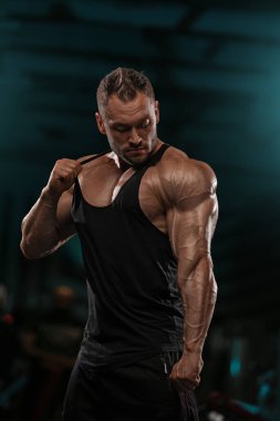 Atletik adam spor salonunda kaslı vücudunu sergiliyor. Çevre, akşam egzersizi sırasında güçlü vücut ve bağlılık sağlığını vurguluyor..