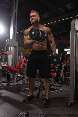 Kendini spora adamış bir adam modern spor salonunda halterleri eğitirken güç gösterisi yapıyor. Odaklanmış ifadesi bağlılığını ve fiziki gelişimini yansıtıyor..