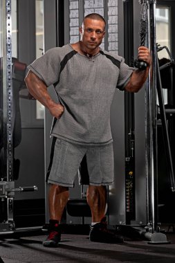 Seçkin fitness sporcusu antrenmana hazırlanırken etkileyici fiziğini sergiliyor. Ayar halter ekipmanları ve yeterli ışıklandırma ile iyi donanımlı bir spor salonu vurguluyor.