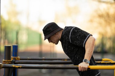 Odaklanmış bireyler spor salonundaki paralel barlarda dalış yaparak spor yapıyor. Sahne güneşli bir günü, temiz bir arkaplan geliştirme atmosferini yakalar.