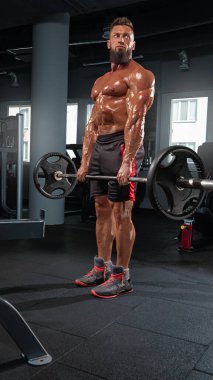 Kaslı adam iyi donanımlı spor salonunda ağırlık kaldırma halteri kullanıyor. Dayanıklılık antrenmanına odaklanıyor. Doğal ışık büyük pencerelerden süzülür.