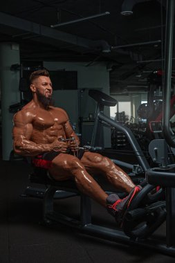 Kaslı adam modern spor salonunda kürek çekme makinesinde egzersiz yapıyor. Fiziksel kondisyonunu ve gücünü geliştirmek için gösterdiği çaba ve adanmışlığa odaklanıyor..