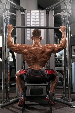 Gündüz vakti modern fitness stüdyosunda ağırlık makinesiyle otururken insan dayanıklılık sergiliyor. Kasları belirgin bir şekilde belirgindir..