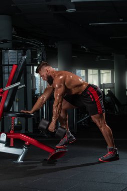 Adanmış sporcular spor salonundaki dambılları kullanarak ağırlık egzersizi yaparlar. Çevrede spor aletleri ve aynalar fitness üzerine odaklanmayı artırıyor.