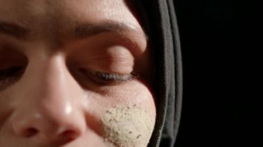 Siyah tesettürlü kadın sanatsal yüz makyajı yapmakla meşgul. Yüzüne odaklanıyor. Karmaşık detaylar ve dokular sergiliyor. Aydınlatılmış yumuşak gün ışığı.