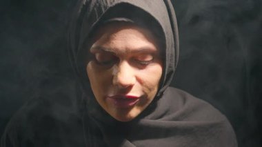 Siyah tesettürlü kadın dumanlı atmosferde sakince düşüncelere dalıp yüzünü yıkıyor. loş ışık dingin ve düşünceli bir ruh hali yaratır yansıma için mükemmel..