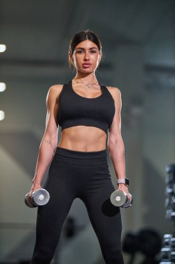 Kararlı kadın antrenman seansında, modern spor salonunda. Dambılları kaldırıyor. Gücünü ve adanmışlığını gösteriyor..