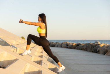 Parlak giysili kadın, gün batımının tadını çıkarırken deniz kenarındaki açık hava yapısına atlıyor. Bu sırada da spor ve genel sağlığına odaklanıyor..