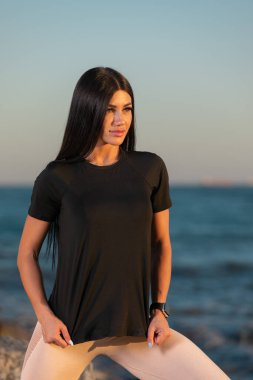 Genç kadın gün batımında etek giyerek ve spor yapmayı teşvik ederek güvenli bir şekilde sahilde duruyor. Huzurlu okyanus arkaplanı refahın yükseltici atmosferini artırır.