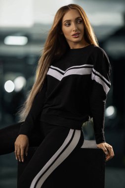 Siyah aktif giyimli beyaz çizgili kadın spor salonunda güven içinde poz veriyor. arka plan bulanık fitness ekipmanları enerjik atmosfer yaratıyor.