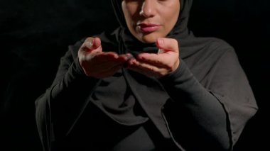 Siyah tesettüre bürünmüş bir kadın ellerini tam önünde uzatıyor ve arka planına siyah kum döküyor. İfadesi iç gözlem ya da maneviyatın daha derin konulardaki düşünceleri davet ettiğini gösteriyor..