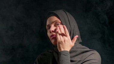 Siyah tesettürlü kadın nazikçe cilt bakımı yapıyor. loş aydınlatma çevre ipuçları gece boyunca dingin ve yansıtıcı ruh hali yaratır..