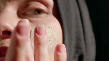 Kadın başörtüsü nazikçe yeşil yüz maskesi takar. Cildini sakin bir ortamda gizler. Kişisel bakım ve rahatlama anını gösterir..