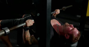 Akşamları spor salonunda bir adam kulaklık takarken göğüs presi egzersizi yapıyor. Halteri kaldırırken konsantrasyon ve çaba gösteriyor..