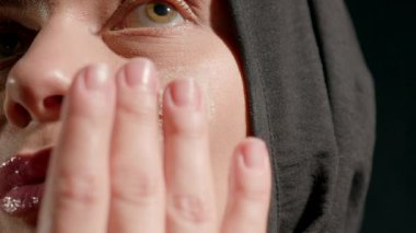 Kadın başörtüsü cilt ürünleri uyguluyor. Yüzü sıcak ve cezbedici iç mekan dekorasyonu yapıyor. Kişisel bakım ve güzellik rutinini sergiliyor..