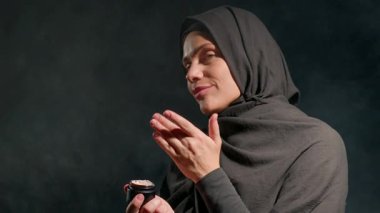 Başörtüsü takan kadın cilt bakımı yapıyor. Kapalı alandaki kendine bakım rutinini yaparken kendine güveni tam ve odaklanmış bir ifadesi var..
