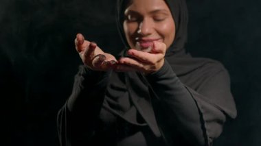 Siyah tesettürlü kadın, elinde toprak tutarak bahçe işleri atölyesindeki mutluluğunu ifade ediyor. Toplum deneyiminin zenginleştirilmesinde diğer katılımcıları kullanıyor..