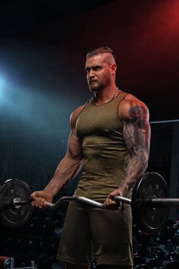 Kaslı bir birey, çağdaş bir spor salonunda biseps kıvrımları için halter kaldırıyor. Çevre, çalışmanın yoğunluğunu vurgulayan canlı ışıklandırma sergiliyor.
