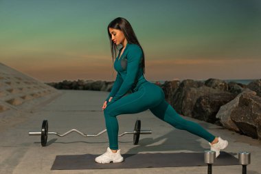 Aktivite kıyafetli kadın bacaklarını Rocky Shore 'un yakınındaki spor salonunda açıyor. Günbatımı, arka planda, huzur veren atmosferde sıcak bir parıltı yaratır..