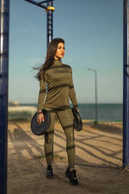 Kadın, deniz kenarında güneşli bir öğleden sonranın tadını çıkarırken yeşil etek giyerek sahilde güven içinde duruyor. Ayarlar zindelik ve canlılık yayar..