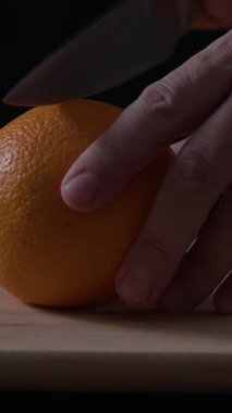 Keskin bir bıçak taze bir portakalı kesiyor ve içindeki sulu eti ortaya çıkarıyor. Dekor, yumuşak ışıklandırmalı, meyvelerin dokusunu ön plana çıkaran rahat bir mutfak..