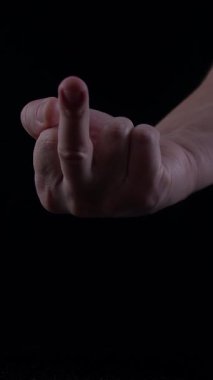 Erkek eli, loş bir ortamda orta parmak hareketi sergiliyor. Güçlü bir meydan okuma ve hayal kırıklığını ifade ediyor..