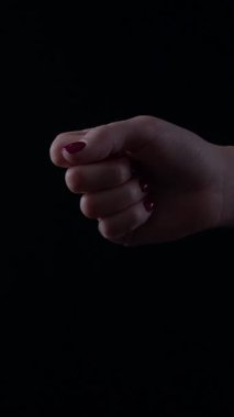 Manikürlü kadın eli yumruk tutarken zarafet gösterir. Ayar, elin zarafetini arttıran koyu bir arkaplan içeriyor. Sahne bir duruş ve güven anı yakalar..