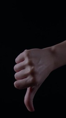 Loş bir ışıkta, bir kadının elini aşağı doğru bir pozisyona indirir ve sonra karşıt duygular taşıyan baş parmaklar yukarı kaldırır..
