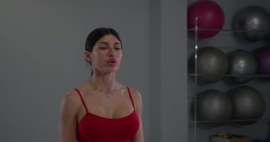 Modern bir fitness stüdyosunda bir kız kendini adamış bir çalışma sırasında esnekliği artırmak ve gerginliği azaltmak için omuz gerer. Parlak ışık odaklanmasını vurguluyor..