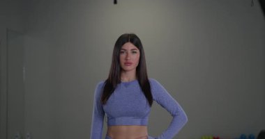 Sportif bir kız kameranın önünde duruyor ve modern bir spor salonunun içinde canlı bir spor etkinliğinde duyuru yapıyor. Onun enerjik varlığı seyirciyi büyülüyor..