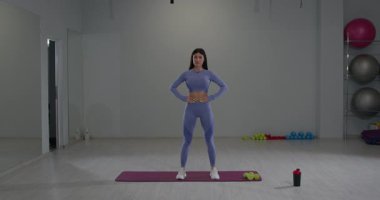 Bir fitness stüdyosunda kendine güvenen bir kadın kollarını başınızın üstüne uzatır ve esnekliği arttırmak ve gerilimi azaltmak için öne doğru eğilir. Parlak alan antrenmanlar için tasarlanmıştır..