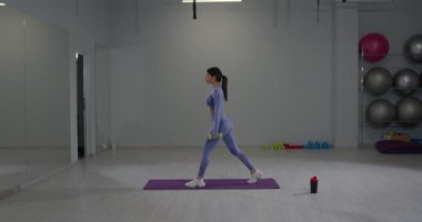 Parlak bir kapalı spor salonunda genç bir kadın Bulgar ataklarına bir spor minderinde biniyor. Ağırlık tutuyor ve odaklanma ve kararlılık gösteriyor..