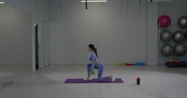 Sportif kız, iyi donanımlı bir fitness stüdyosundaki halterleri kullanarak Bulgarca hamleler yaparken formuna odaklanıyor. Atmosfer parlak ve enerjik, sağlıklı bir yaşam tarzını destekliyor..