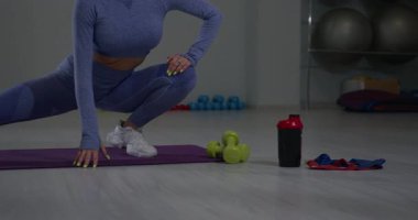 Sporcu kız spor salonunda yan yana hamleler yapıyor. Renkli ağırlık ve direnç bantları yakınlarda ilham verici bir atmosfer yaratırken o formuna odaklanıyor..