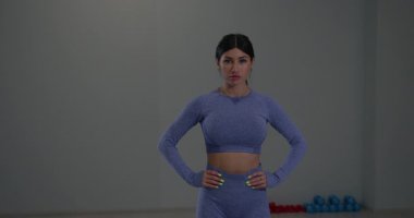 Genç atletik kadın, iyi aydınlatılmış bir spor salonunda yan yana hareket ediyor. Formunu geliştirmek ve genel olarak formda kalmak için odaklanır..