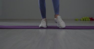 Sportif kız, mor bir egzersiz paspasının üzerinde durarak ayaklarını esnetmeye odaklanmış. Parlak spor salonu, sabah egzersizi için enerjik bir atmosfer yaratıyor..