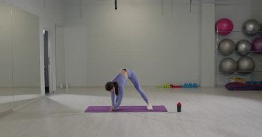 Bir fitness stüdyosunda atletik bir kız, odaklanma ve esneklik göstererek vurgun yapar. Arka planda egzersiz ekipmanlarıyla aydınlık bir şekilde aydınlatılan bu sahne, onun ithafını yakalıyor..