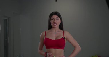 Sportif kız sunucu şık bir stüdyoda enerjiyle kameraya doğru konuşuyor. Onun atletik kıyafeti ve hareketli tavırları dikkat çeker ve odaklanır..