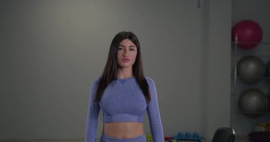 Sportif bir kız spiker, iyi donanımlı bir fitness stüdyosunda şık spor giysileri giyerken kameraya güvenle konuşuyor. Atmosfer motivasyon ve enerjiyi yansıtır..