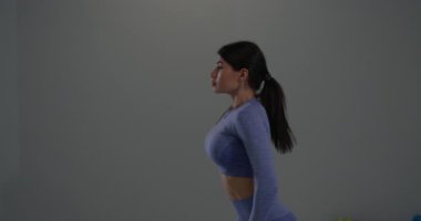 Atletik kız esnekliği artırmak için öne eğilme egzersizi yapıyor. İçerde iyi aydınlatılmış bir ortamda sağIık ve zindelik hedeflerini destekleyen odaklanma ve güç sergiliyor..