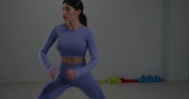 Sporcu kız hareketlerini sağa sola kaydırarak spor salonu ortamında güç ve çeviklik göstererek hamlelerle meşgul. Odaklanmış ve kararlı..