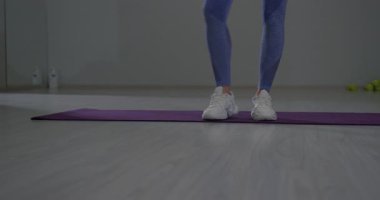 Sportif kız spor salonundaki mor bir paspasın üzerinde ayak esnemesini gösteriyor. Bu aktivite esnekliği ve egzersiz için uygun ısınma tekniklerini vurgular..