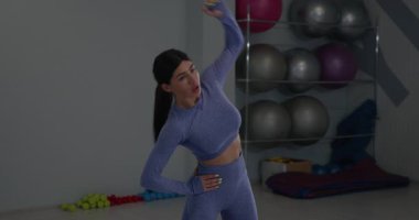 Sporcu kız spor salonlarında sağa sola eğiliyor ve dinamik esneme hareketleri yapıyor. Forma uygun bir kıyafet giyip spor ve sağlığa olan bağlılığını gösteriyor..