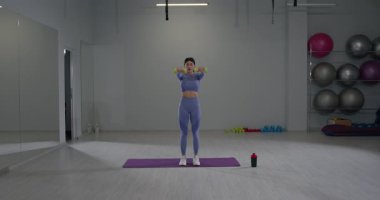 Sportif kız iyi aydınlatılmış bir spor salonunda parlak ağırlıklarla omuz egzersizleri yapıyor. Odaklanmış ve idman kıyafetleri içinde antrenman sırasında güç ve kararlılık gösteriyor..