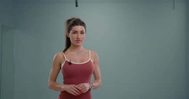 Spiker, hafif bir stüdyoda seyircilere coşkuyla sesleniyor. Spor kıyafetleri giyiyor ve spor haberleri ya da güncellemeleri sunmaya hazır görünüyor..