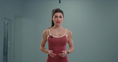 Sportif kız spiker doğrudan kameraya konuşuyor fitness ipuçlarını paylaşıyor ve seyircilerle iletişim kuruyor. Modern bir stüdyoda kendine güveni ve enerjisi ile duruyor..