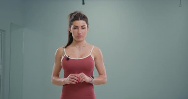 Sportif kız sunucu doğrudan kameraya konuşuyor. Modern fitness stüdyosunda atletizm ve çekiciliğini gösteriyor. Sağlık ve sağlığa odaklı aktif bir bölümde..