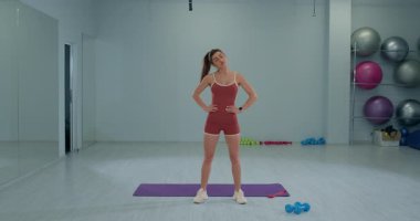 Kız sporcu spor salonunda başını sağa sola eğerek duruyor. Uygun bir kıyafet giyiyor ve ısınma rutinine hazırlanırken odaklanmış görünüyor..
